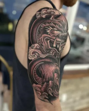 Ornamental black and grey dragon half sleeve wrapping the upper arm — by Adam Crane