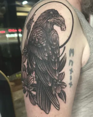 Black and grey raven perched below a full moon on an upper arm — by Adam Crane