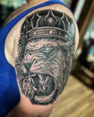 Black and grey roaring lion wearing a jewelled crown on a shoulder — by Adam Crane