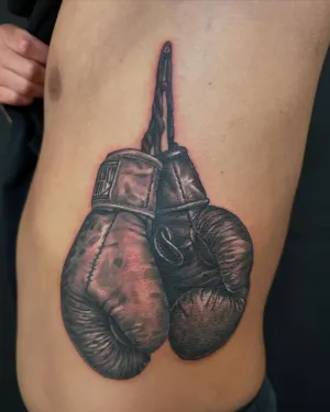 Black and grey boxing gloves hanging from their laces, on the ribs — by Adam Crane