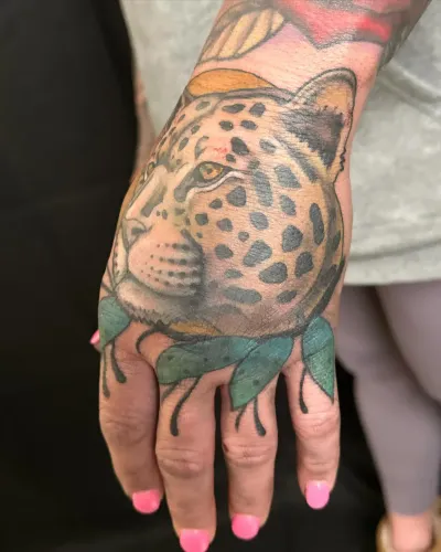Colour leopard face tattooed across the back of a hand — by Adam Crane at Ministry Ink