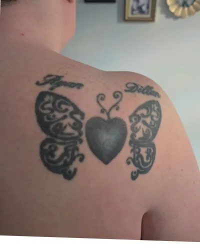 Fine line butterflies either side of a heart locket with script names, upper back — by Adam Crane at Ministry Ink