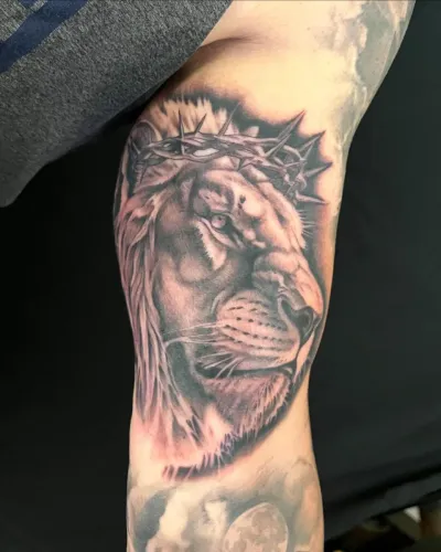 Black and grey lion wearing a crown of thorns on an inner arm — by Chay Menke at Ministry Ink