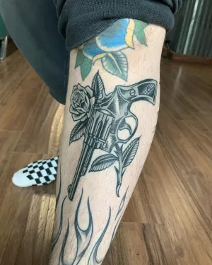 American traditional revolver and roses tattooed down a shin — by Chay Menke