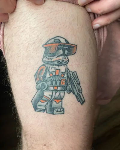Colour armoured toy soldier figure tattooed on a thigh — by Chay Menke at Ministry Ink