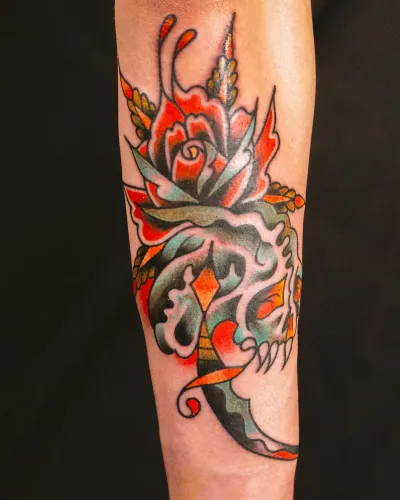 American traditional roses and foliage in orange and green on a forearm — by Chay Menke at Ministry Ink