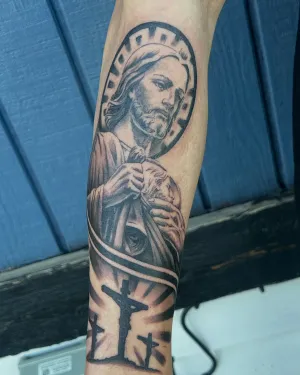 Black and grey religious forearm sleeve with a saint and a cross — by Gabriel Gonzalez